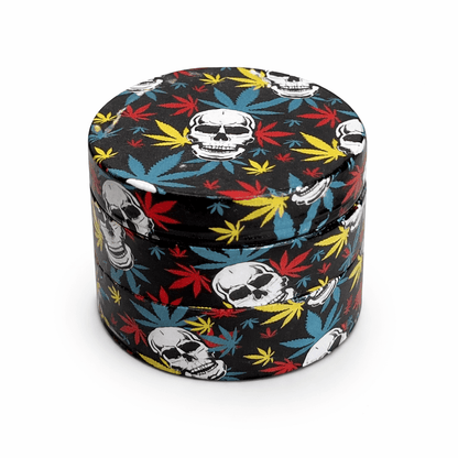 Grinder CBD Skull 4 parties métal imprimé – motifs têtes de mort et feuilles cannabis multicolores fond noir, broyeur herbes résistant dents acier, accessoire CBD pas cher livraison France