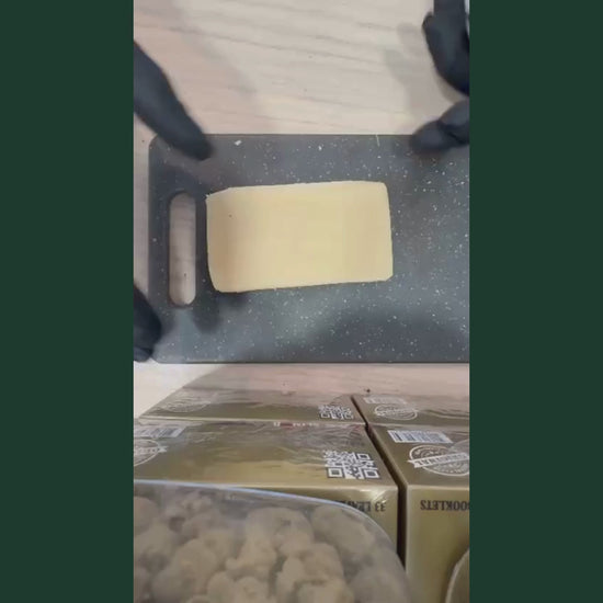 Video de demonstration de l'ice hash CBD : bloc de resine CBD de couleur jaune dore translucide, texture lisse et dense, tenu et coupe avec un cutter par des mains gantees de noir sur un plan de travail gris anthracite. Packagings de produits CBD visibles en arriere-plan. Ice hash CBD puissant disponible a l'achat sur CBD Pas Cher 14, livraison France, taux THC inferieur a 0,3%.