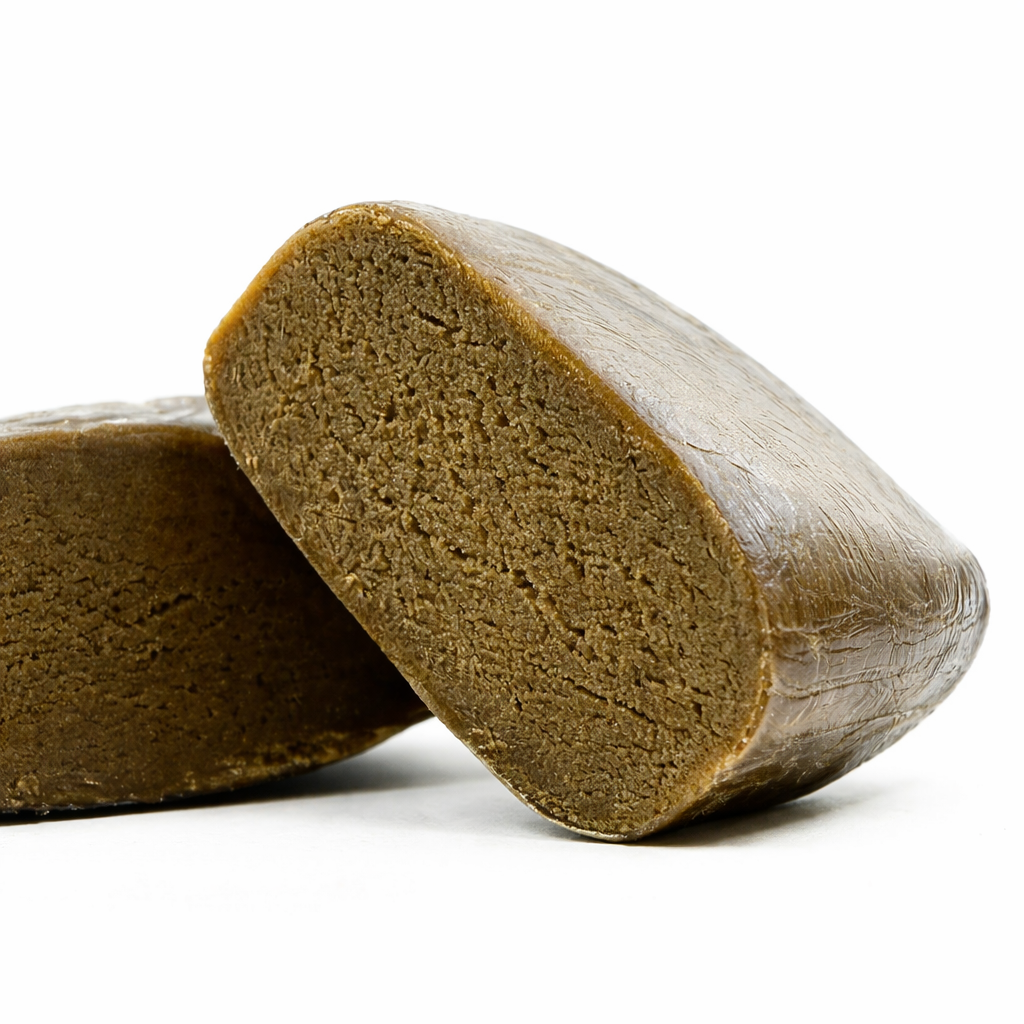 Deux blocs de resine CBD CSA Piatella hash premium photographiés en gros plan angle rasant, fond blanc uni. Bloc de gauche coupe nettement revelant l'interieur brun dore homogene a texture granuleuse dense et compacte. Bloc de droite entier avec croute exterieure lisse brun fonce presque noire, surface craquelée avec reflets cireux. Coupe franche visible en premier plan. Hash concentre premium THC legal 0,3%, CBD Pas Cher 14, livraison France.